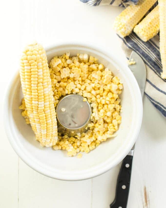 cutting corn off the cob in a white bowl