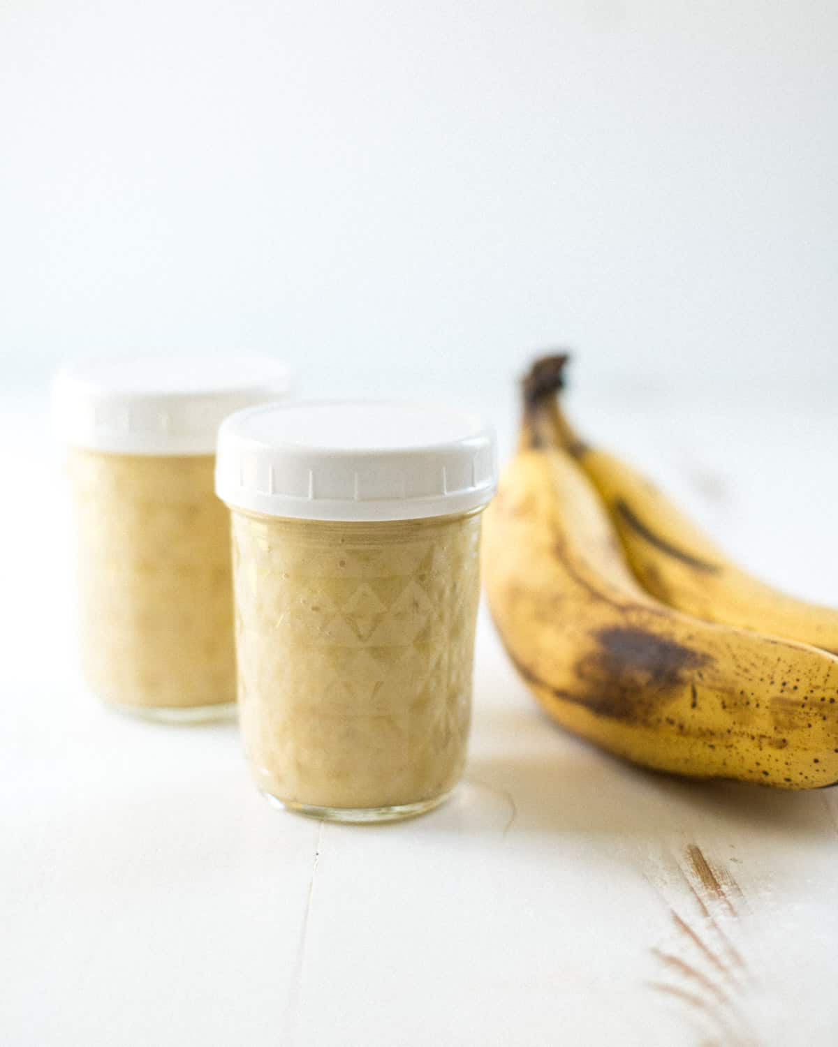 a banana and 2 glass jars on a white table