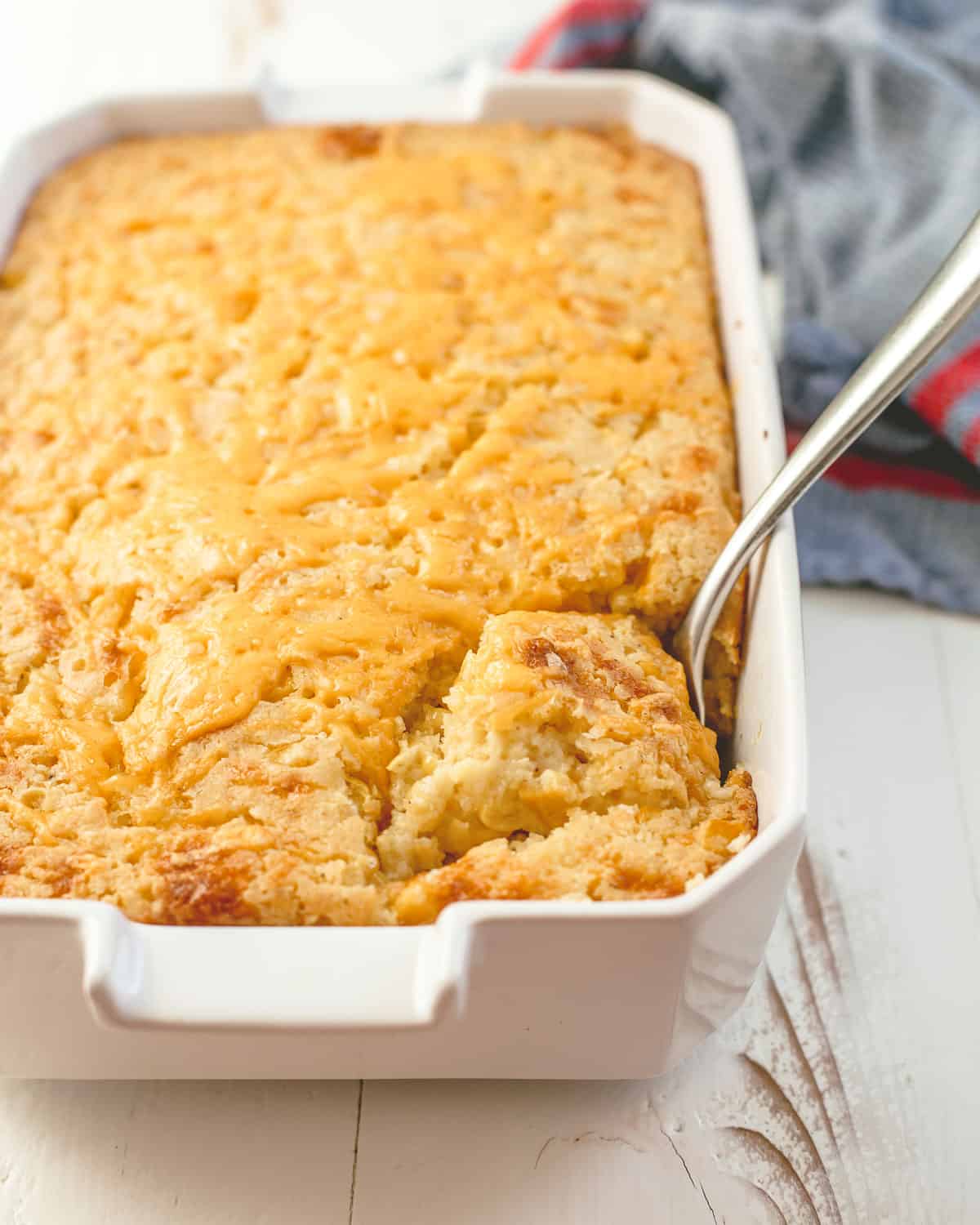 a spoon in corn casserole in a white baking dish