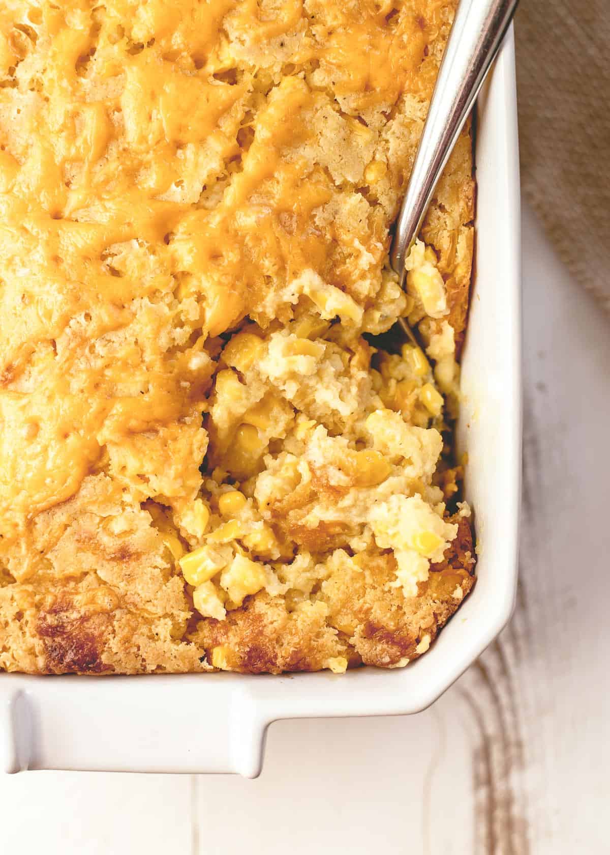 a spoon in corn casserole in a white baking dish