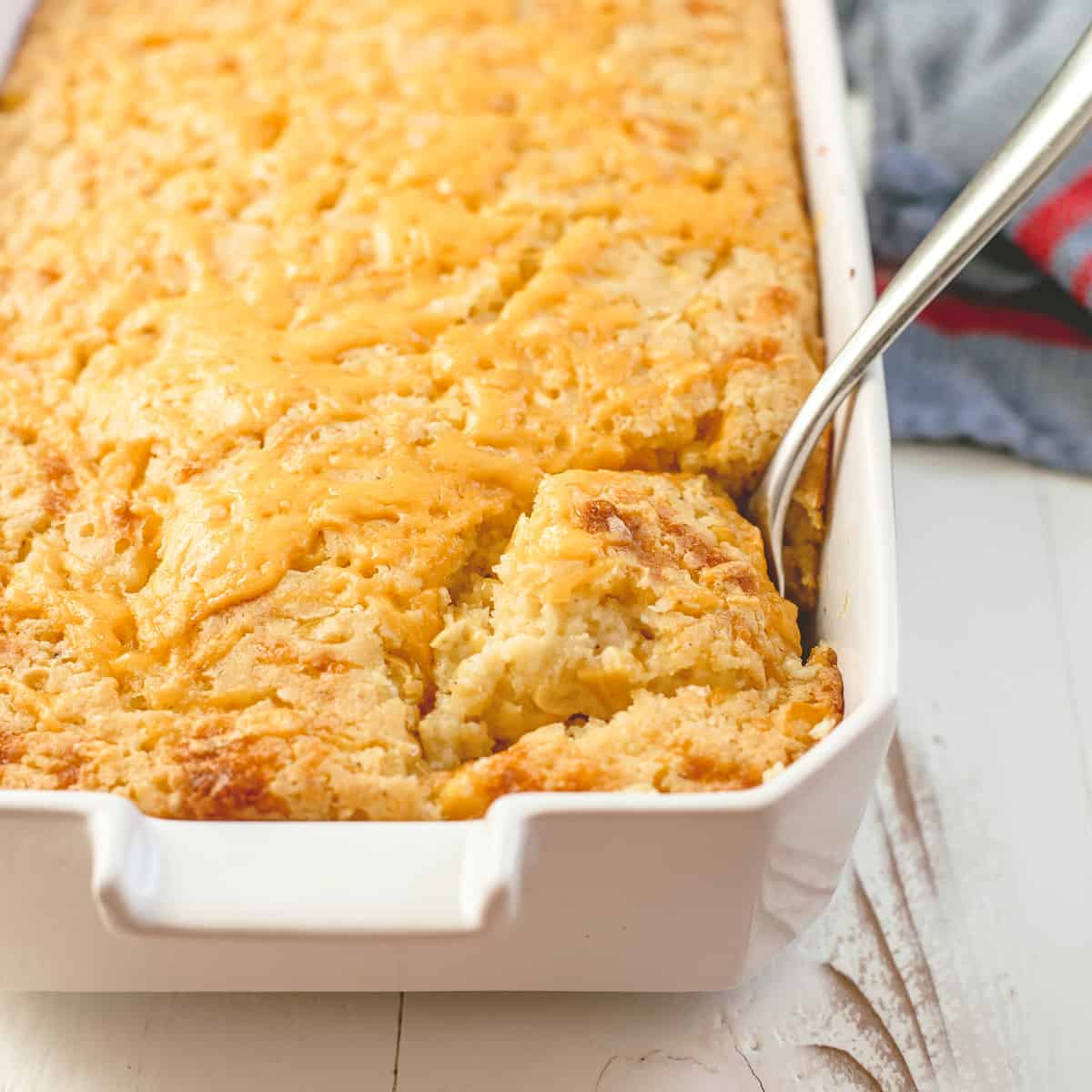 a spoon in corn casserole in a white baking dish