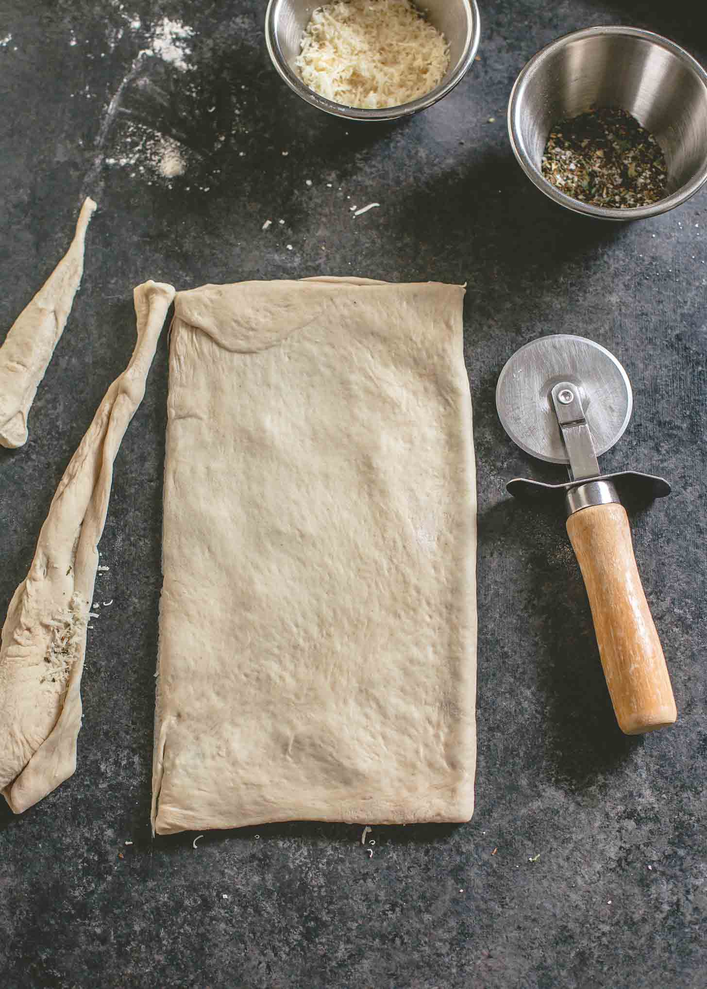 overhead image of cutting raw pizza dough with a pizza cutter