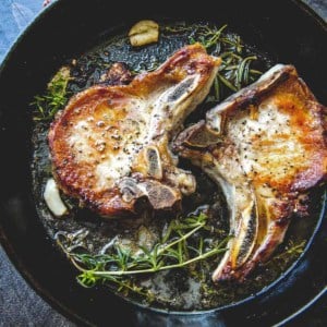 pork chops cooking in a cast iron pan with herbs