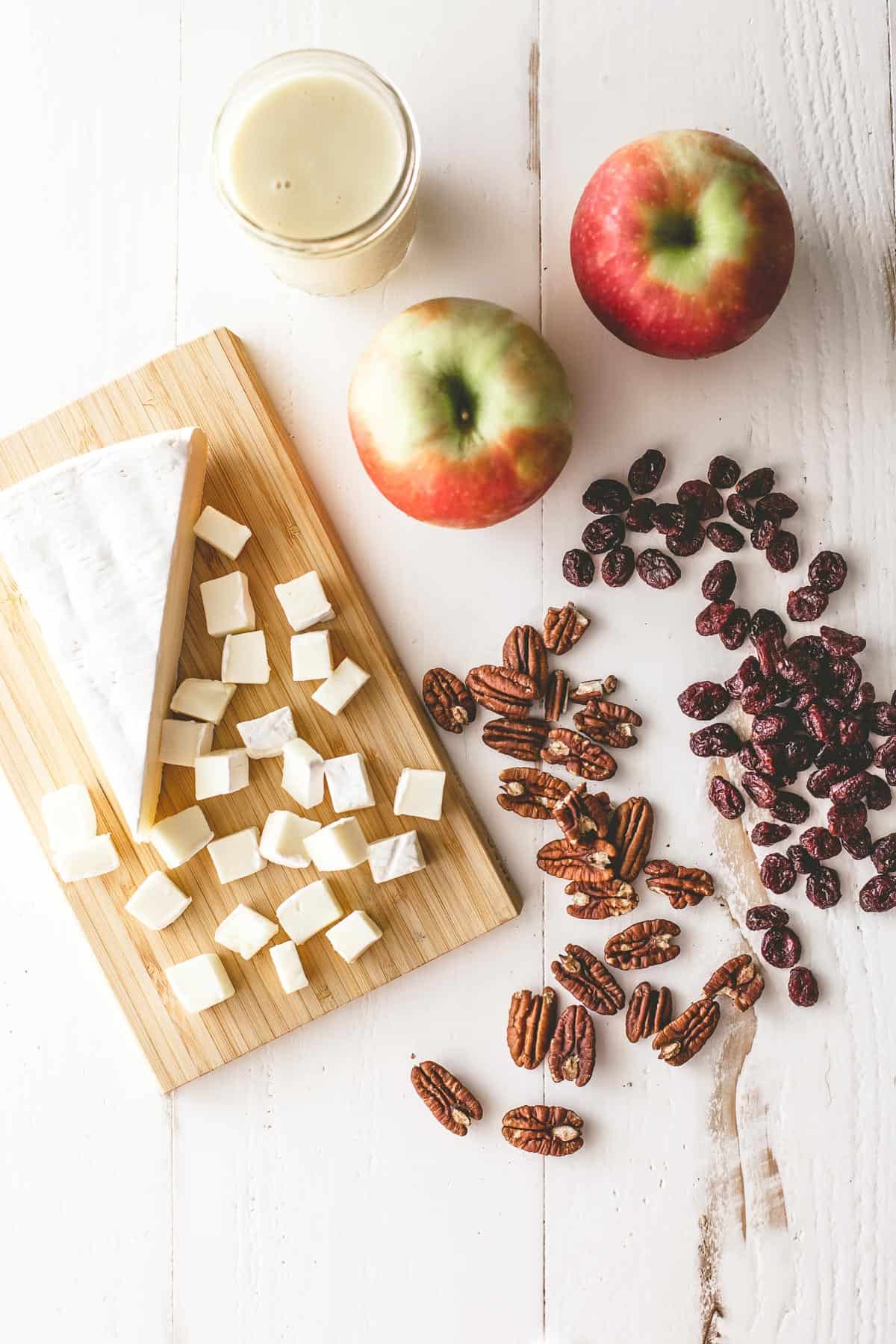 overhead image of cheese, apples and nuts on a white table