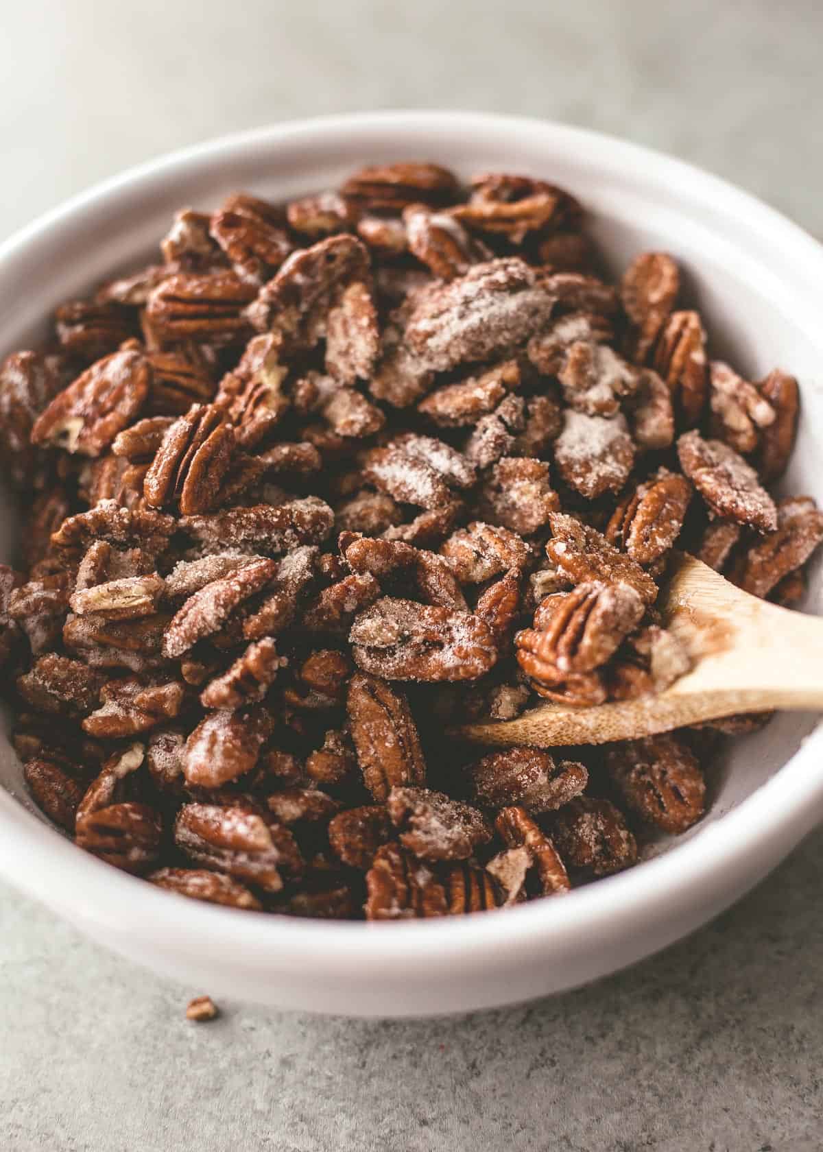 tossing pecans in a bowl with a wooden spoon