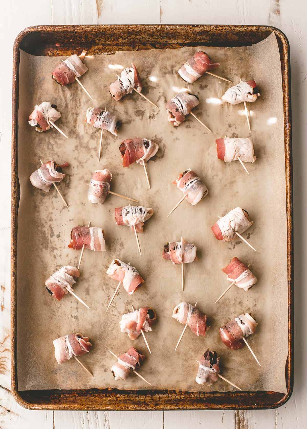 dates wrapped in uncooked bacon on a sheet pan