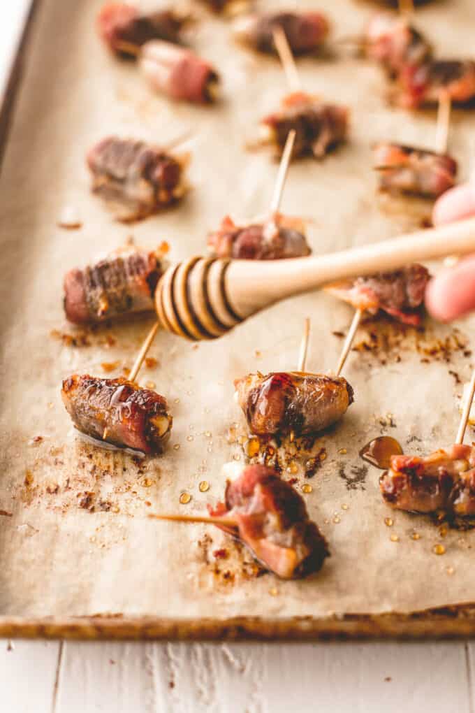 drizzling honey on bacon wrapped dates on a parchment lined sheet pan