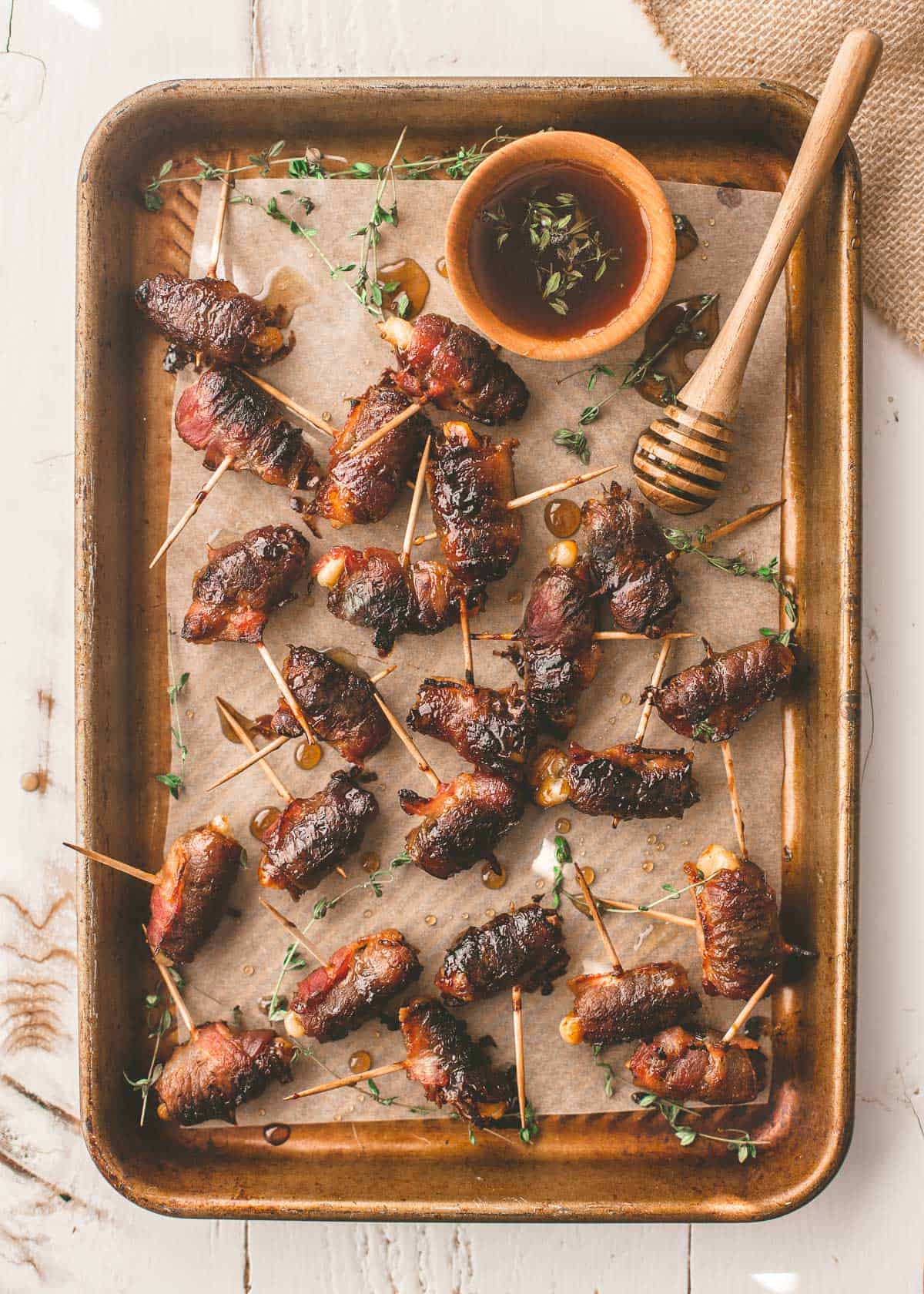 bacon wrapped dates on a parchment lined sheet pan with thyme sprigs