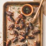 bacon wrapped dates on a parchment lined sheet pan with thyme sprigs