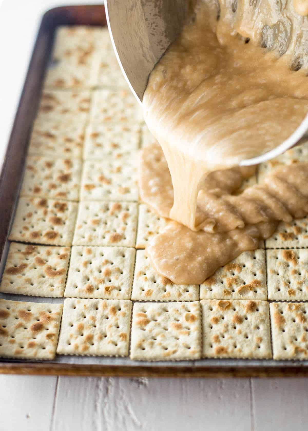 adding toffee mix to saltines on a sheet pan