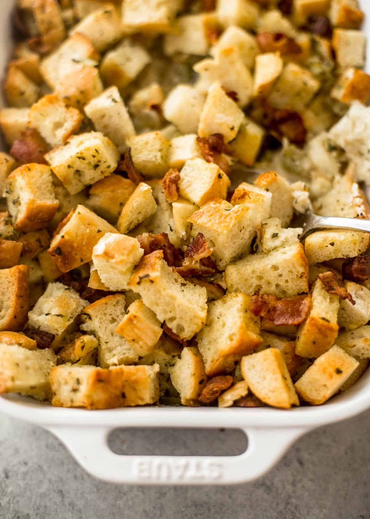 stirring cubed bread in a white baking dish