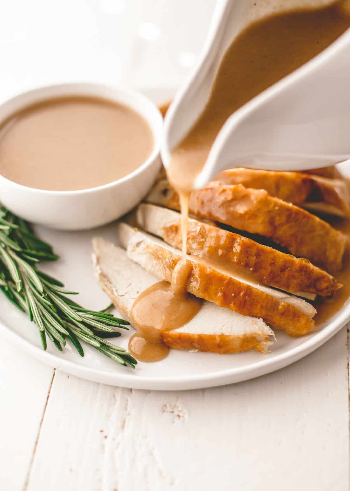 pouring gravy over turkey slices on a white plate