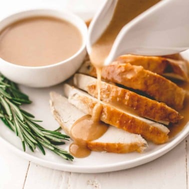 pouring gravy on turkey slices on a white plate
