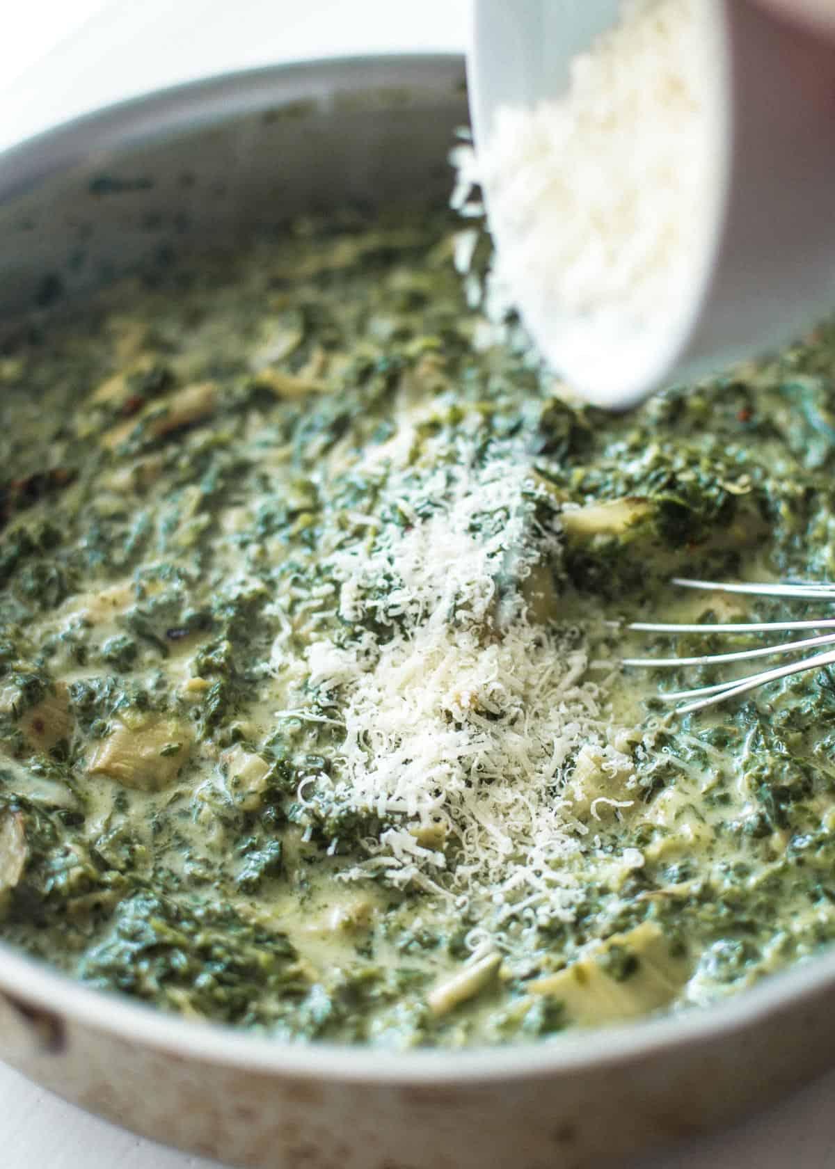 adding spinach and parmesan to skillet with artichokes