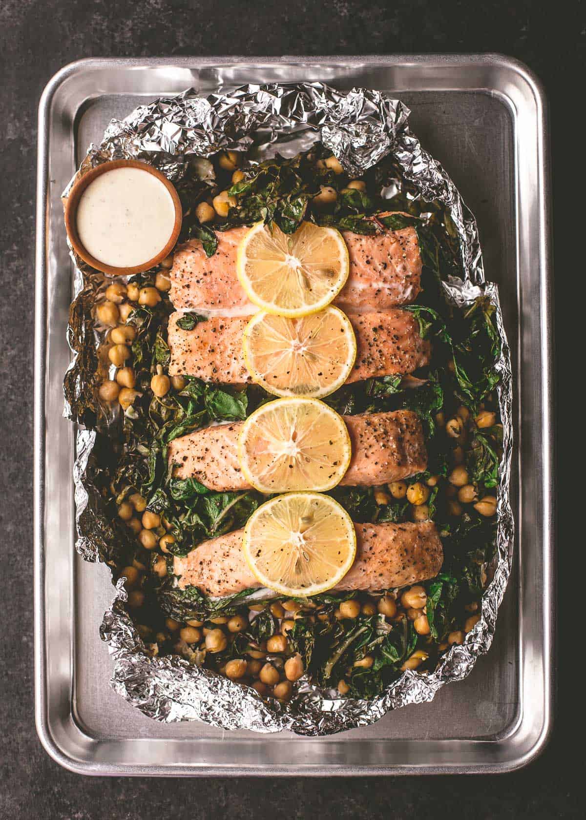 salmon and greens with sauce in foil on a sheet pan