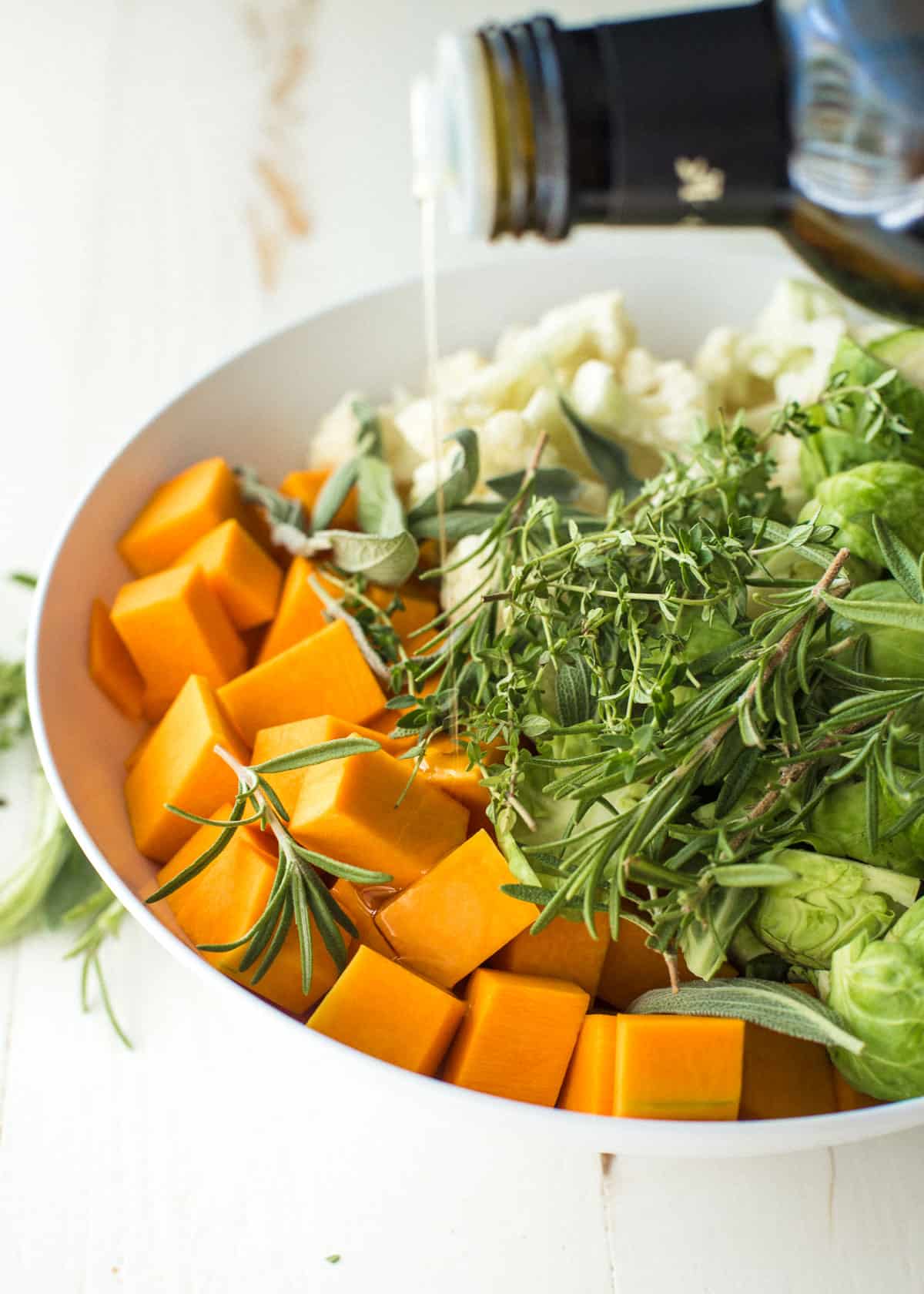 drizzling oil over herbs and raw vegetables in a white bowl