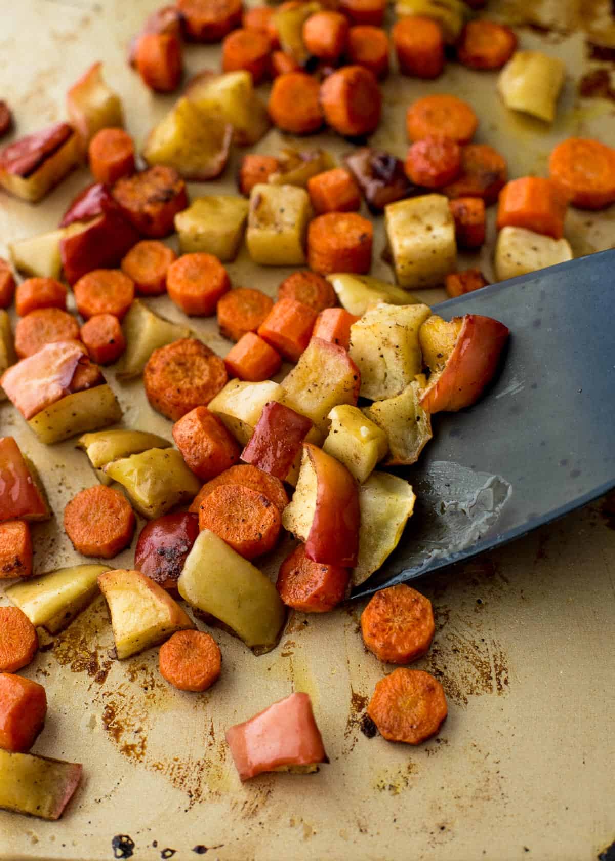 using a spatula to stir roasted vegetables on a sheet pan