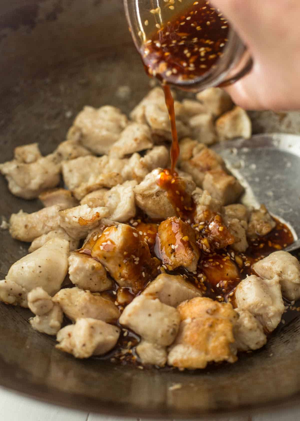 adding sauce to the chicken in a wok