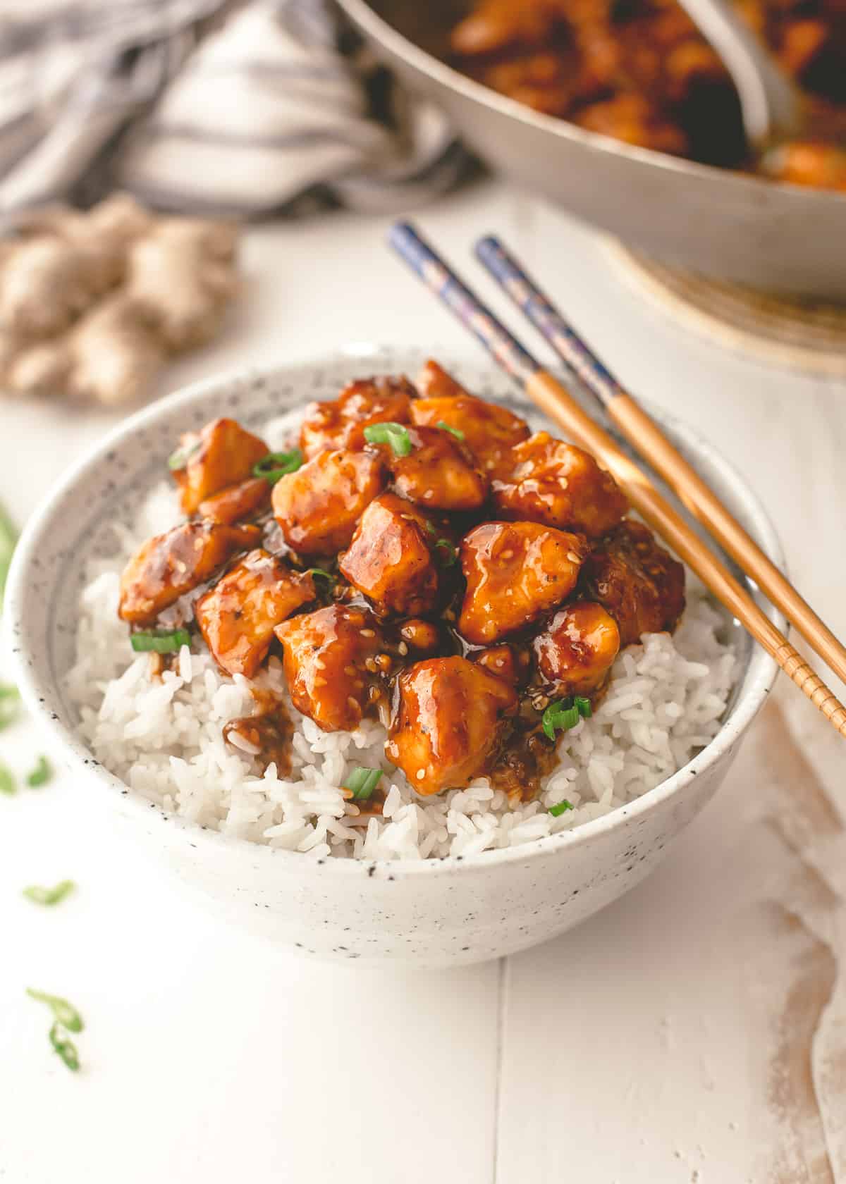 chicken stir fry over rice in a white bowl with chopsticks