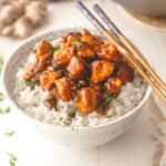 stir fry over rice in a white bowl with chopsticks