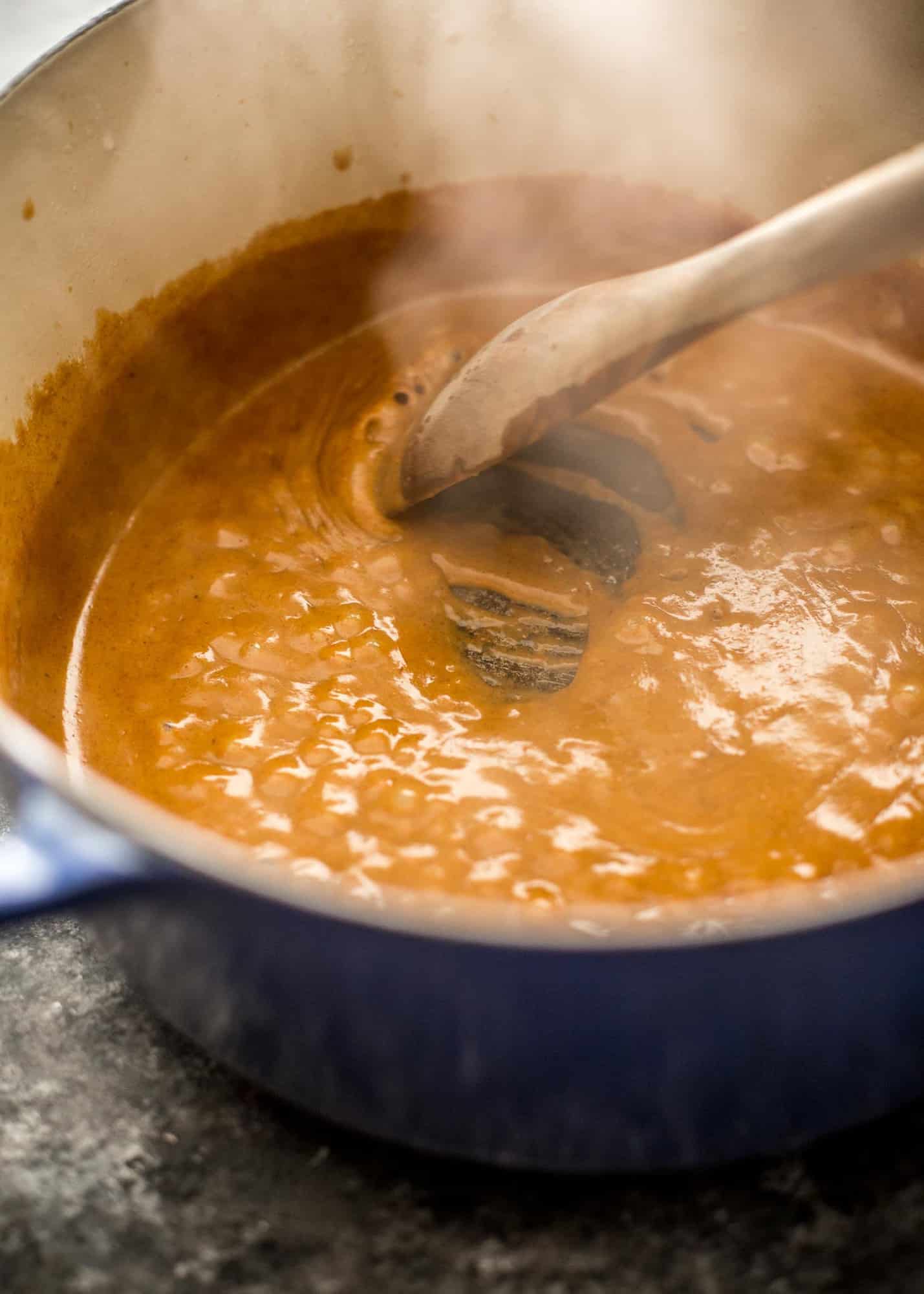 stirring curry paste in a blue dutch oven