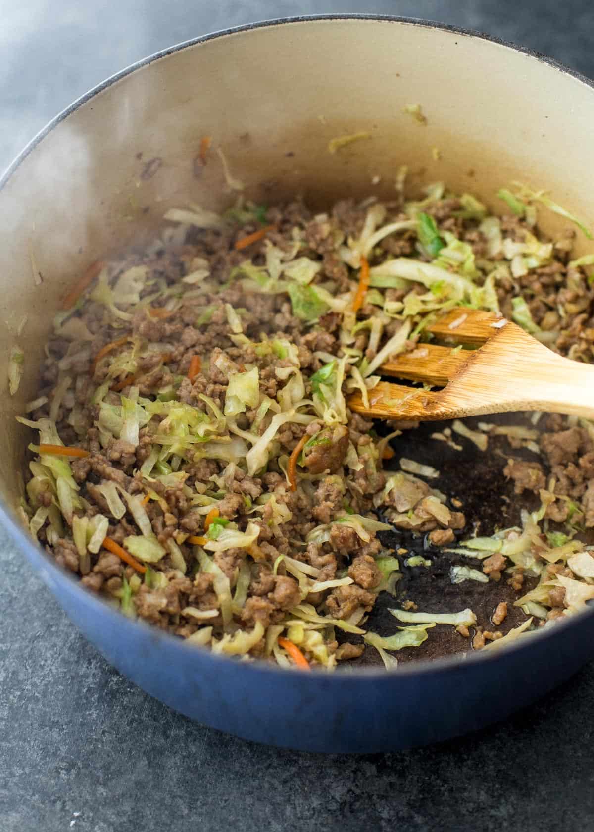 stirring filling for spring rolls in a blue dutch oven