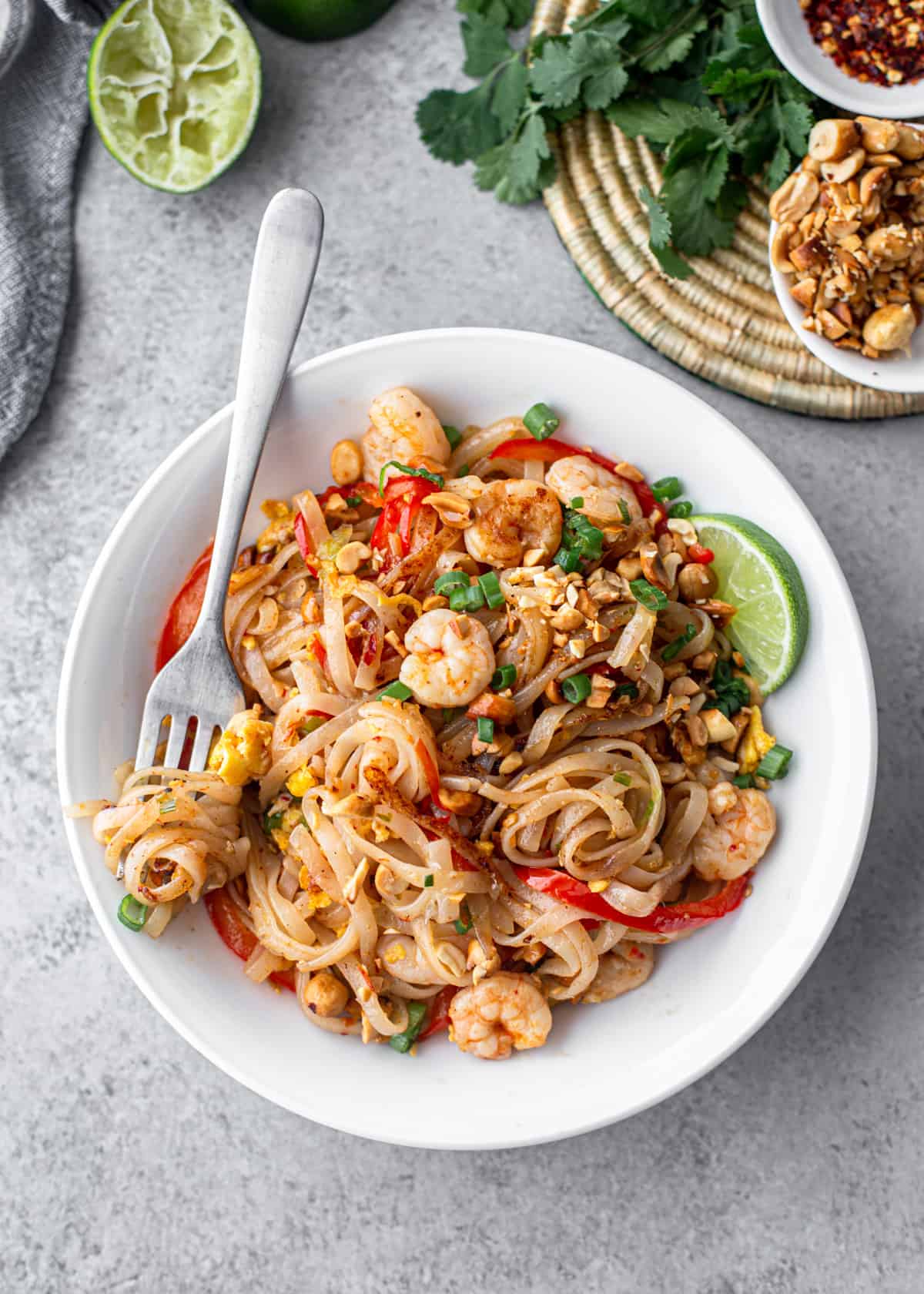 pad thai with peppers and shrimp in a white bowl on a grey countertop