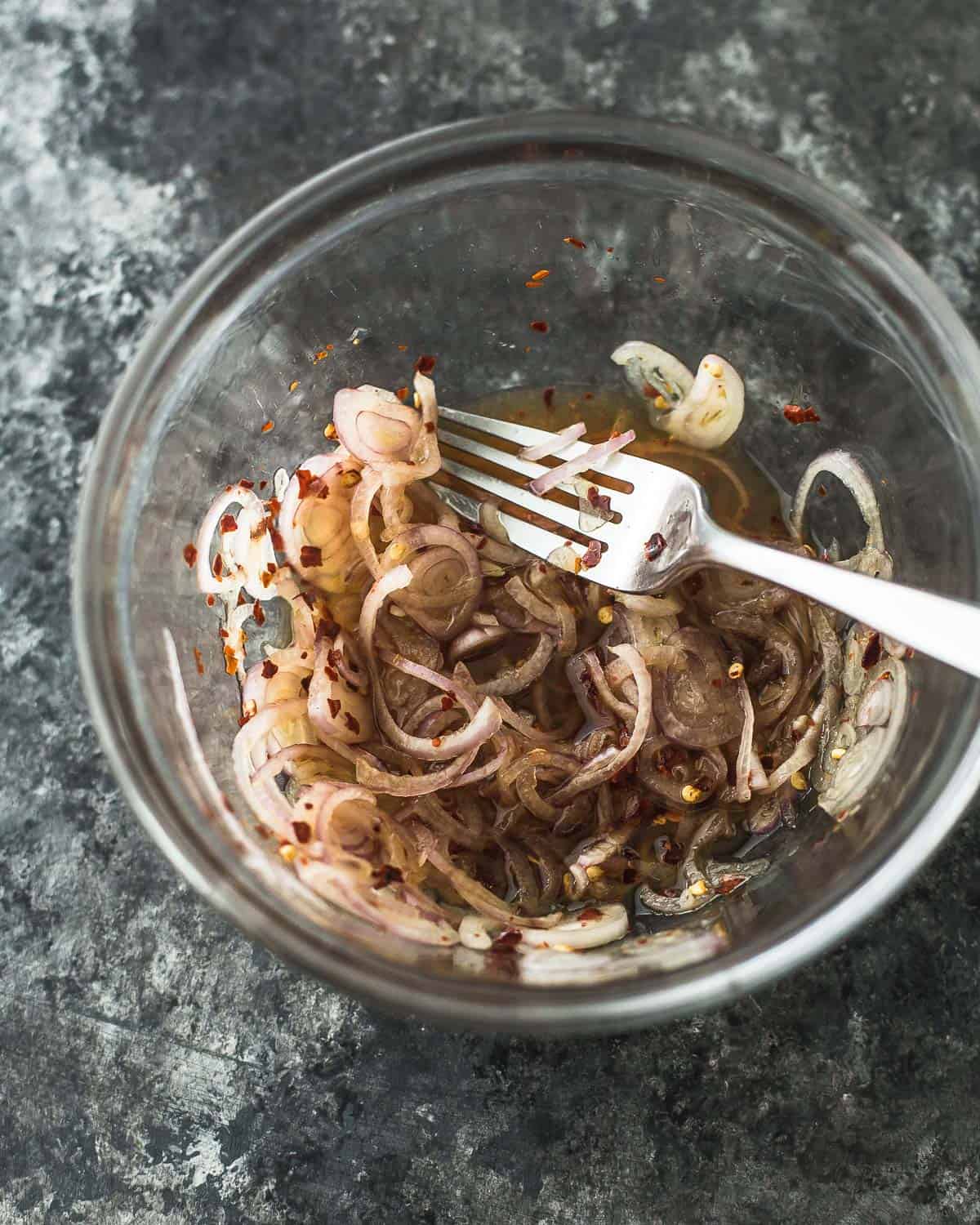 overhead image of shallots and dressing in a clear glass bowl