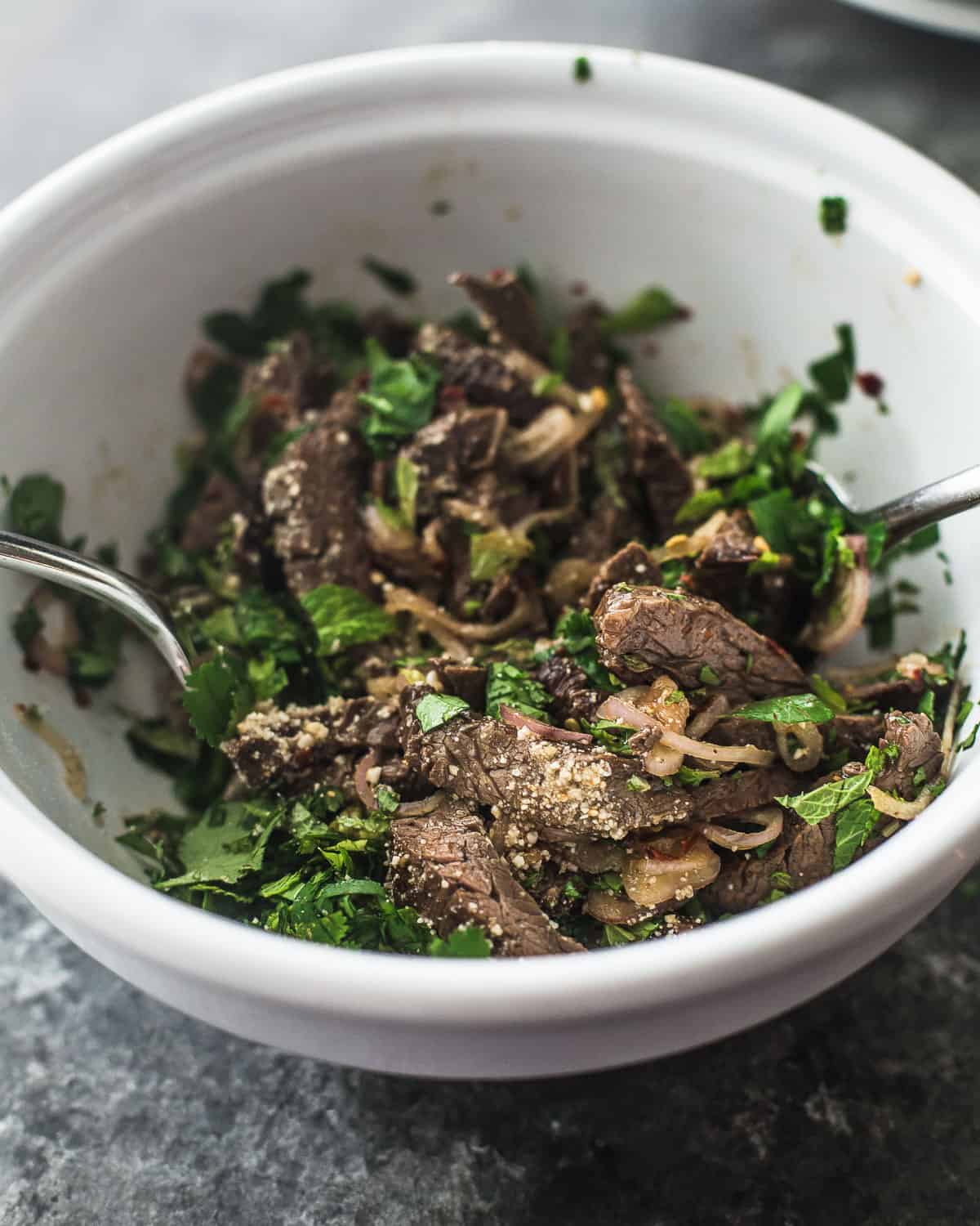 stirring steak and herbs in a white bowl