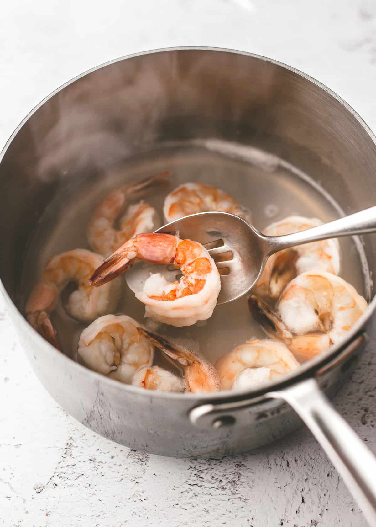 overhead image of a spoon holding a cooked shrimp over a saucepan