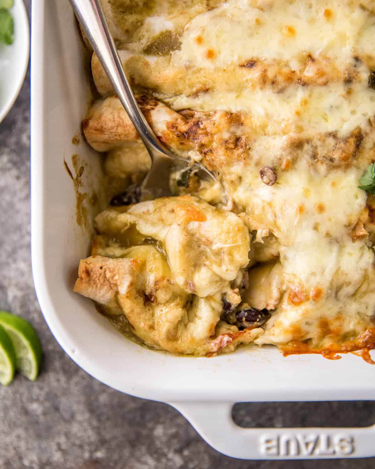 an overhead image of a spoon in a white dish of enchiladas