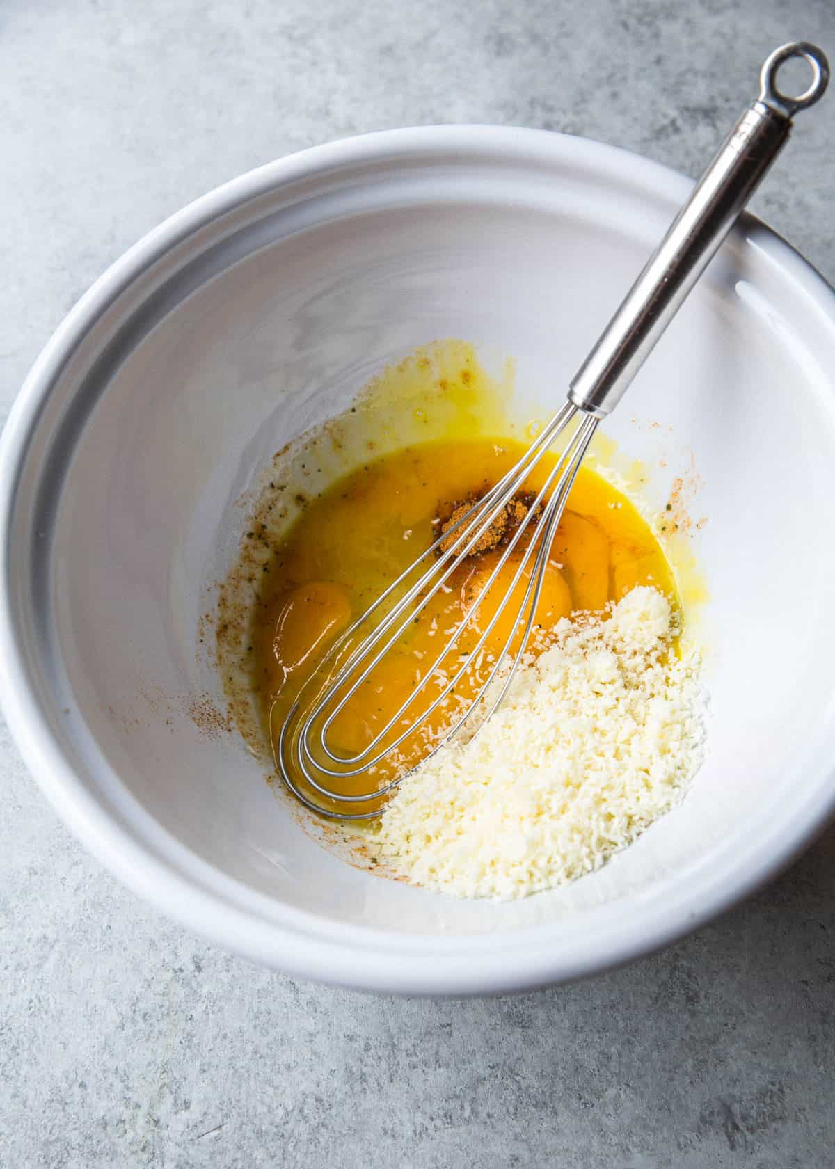 stirring eggs in a white bowl with a whisk