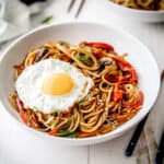 sesame vegetable noodles topped with a fried egg in a white bowl