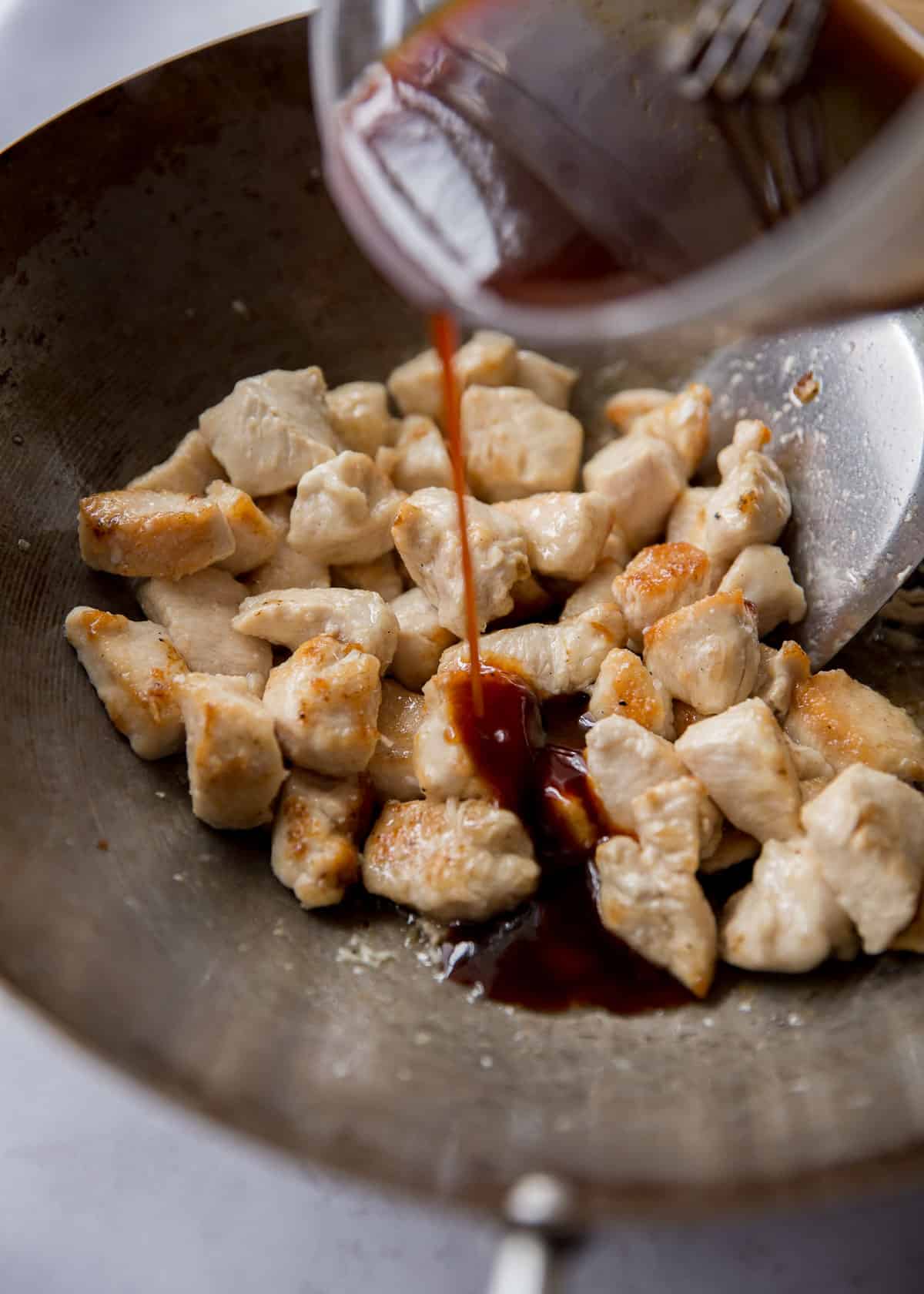 adding sauce to chicken in a wok