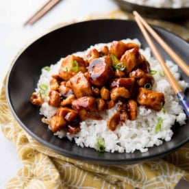 chicken and rice in a black bowl with chopsticks