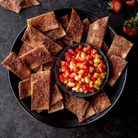 baked cinnamon chips and a bowl of fruit salsa on a black tray