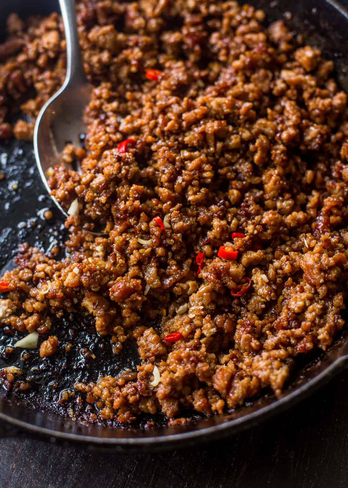 overhead image of a spoon stirring ground pork in a skillet