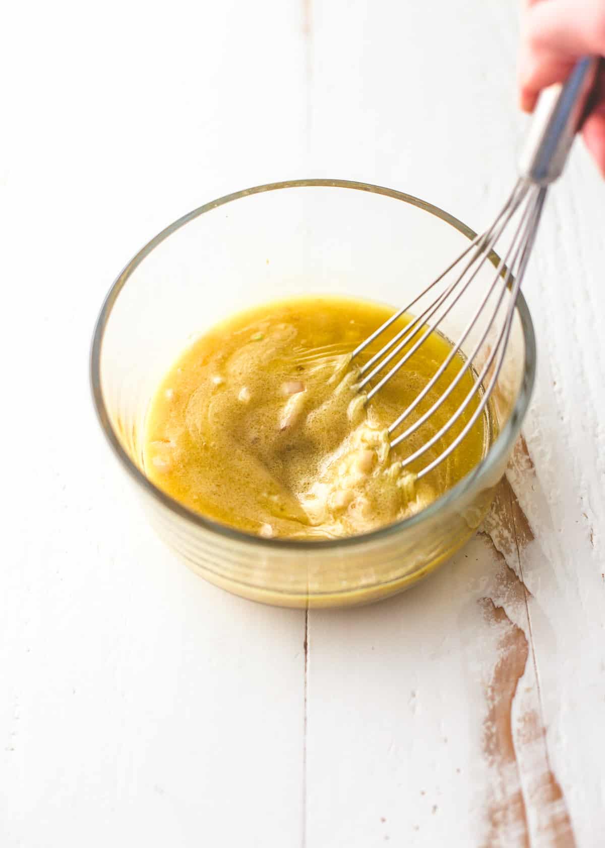 mixing dressing in a clear bowl with a whisk