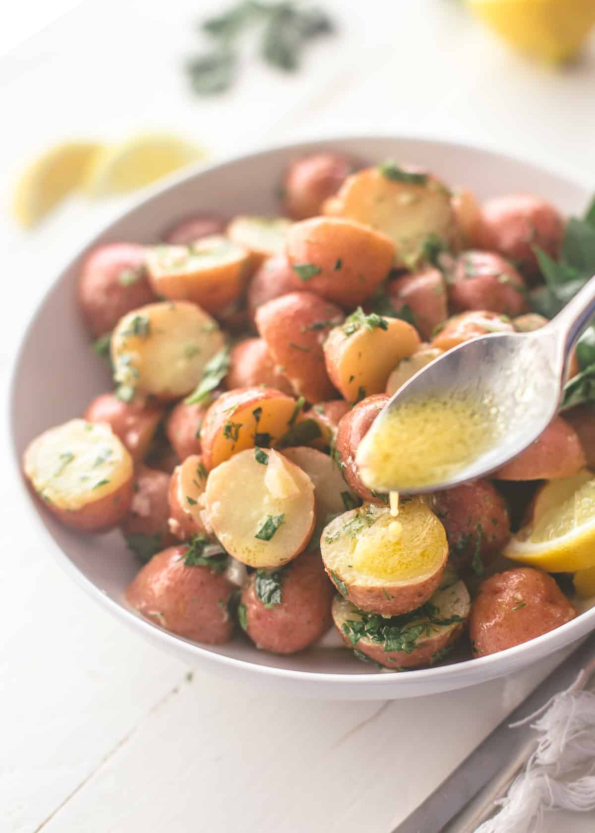 drizzling dressing over red potatoes in a white bowl