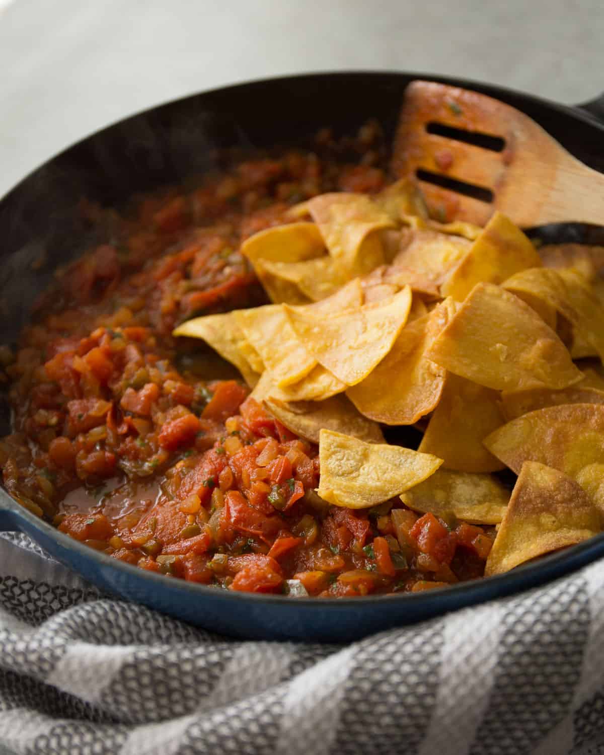 stirring baked tortilla chips into tomatoes in a cast iron skillet