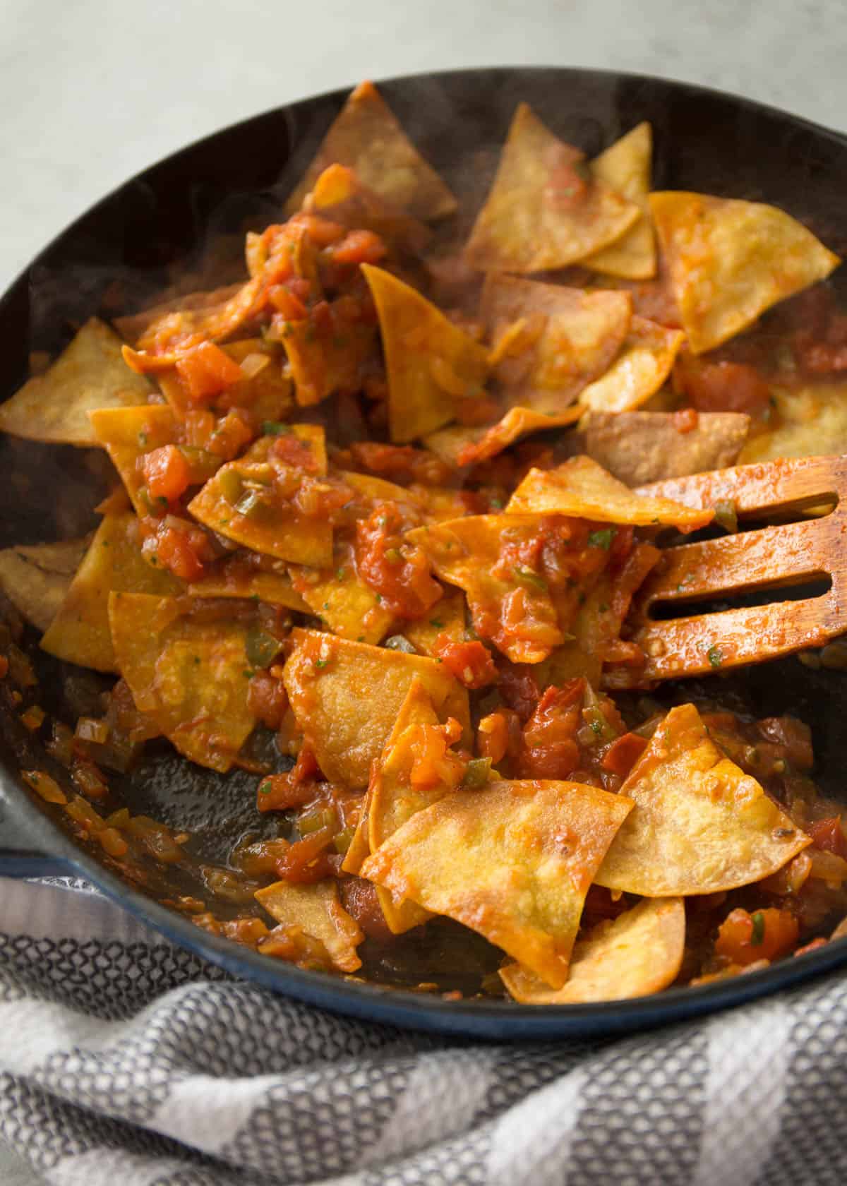 stirring baked tortilla chips into tomatoes in a cast iron skillet