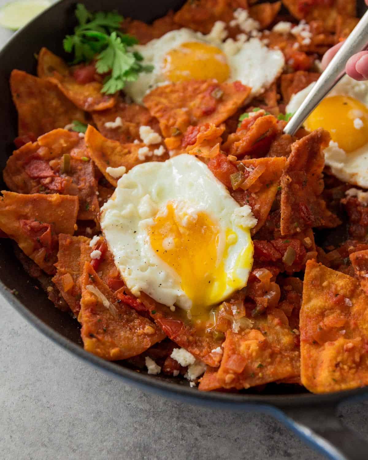 fried eggs on top of tomato covered tortilla chips in a cast iron skillet