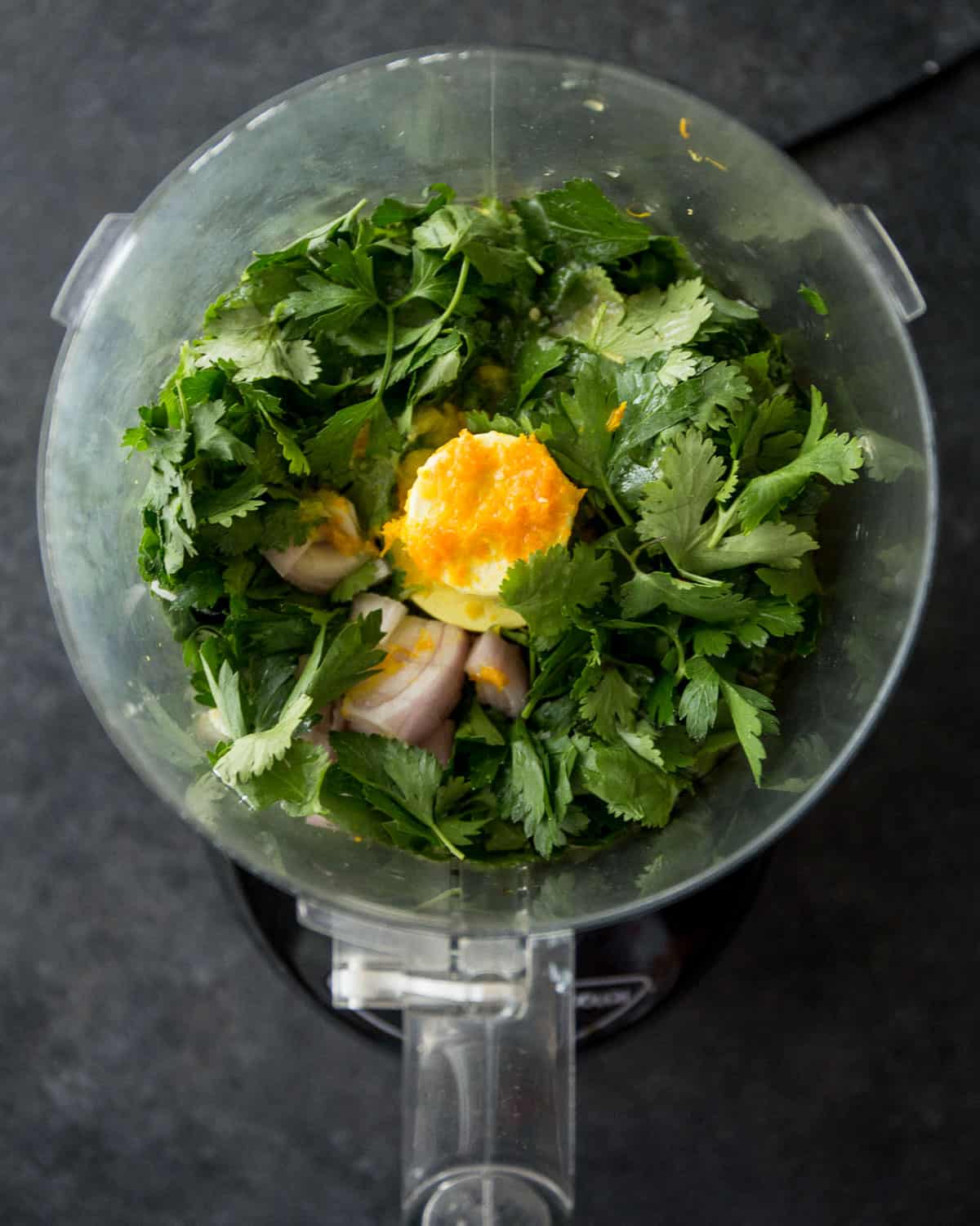 overhead image of herbs and garlic with citrus in a food processor