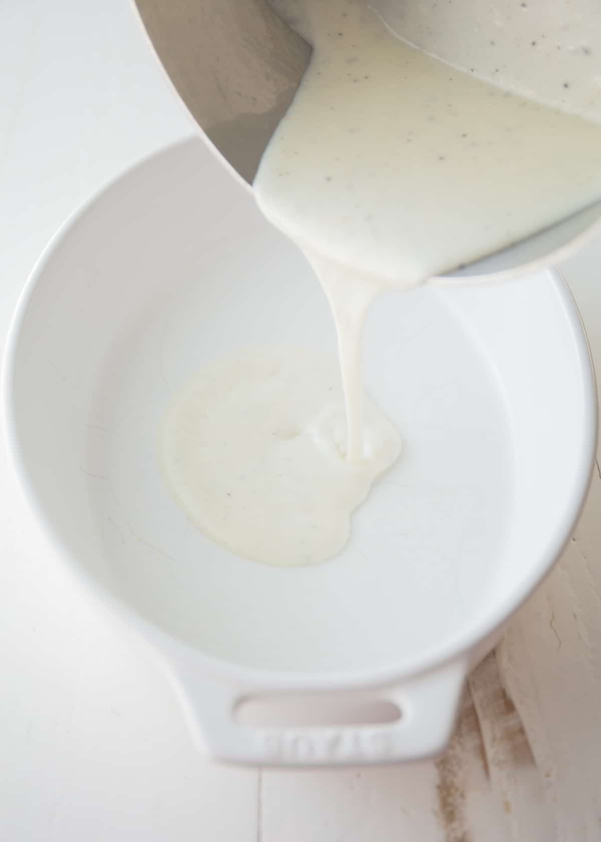 adding bechamel into the bottom of a white baking dish