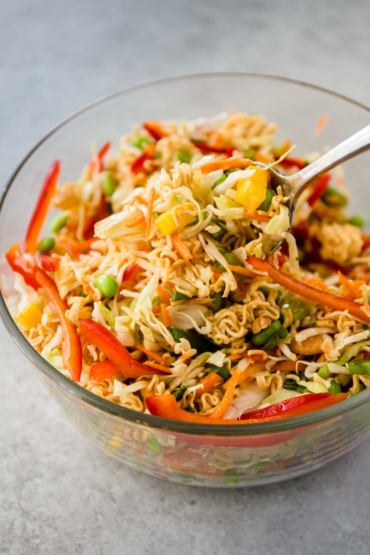 a spoon in a clear bowl of crunchy ramen salad