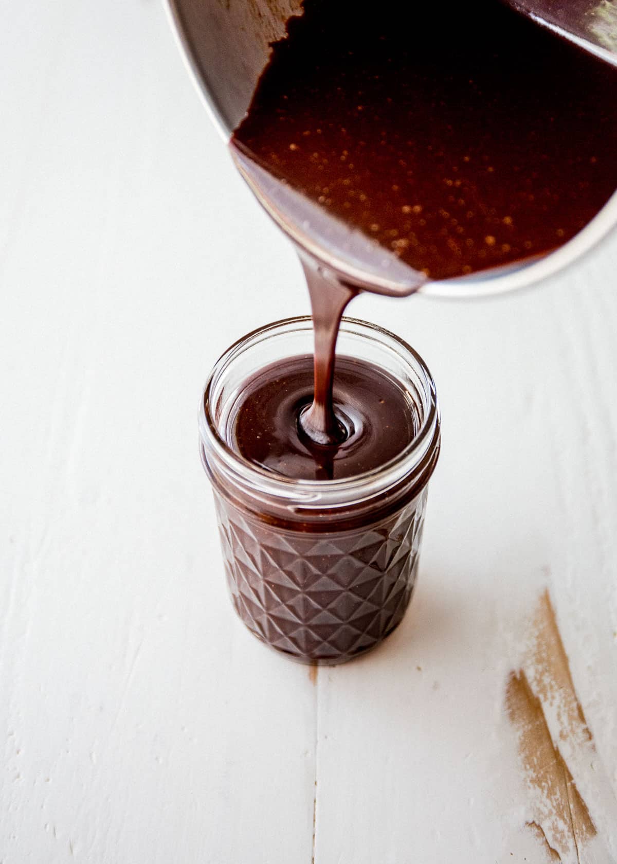 pouring hot fudge into a small glass jar