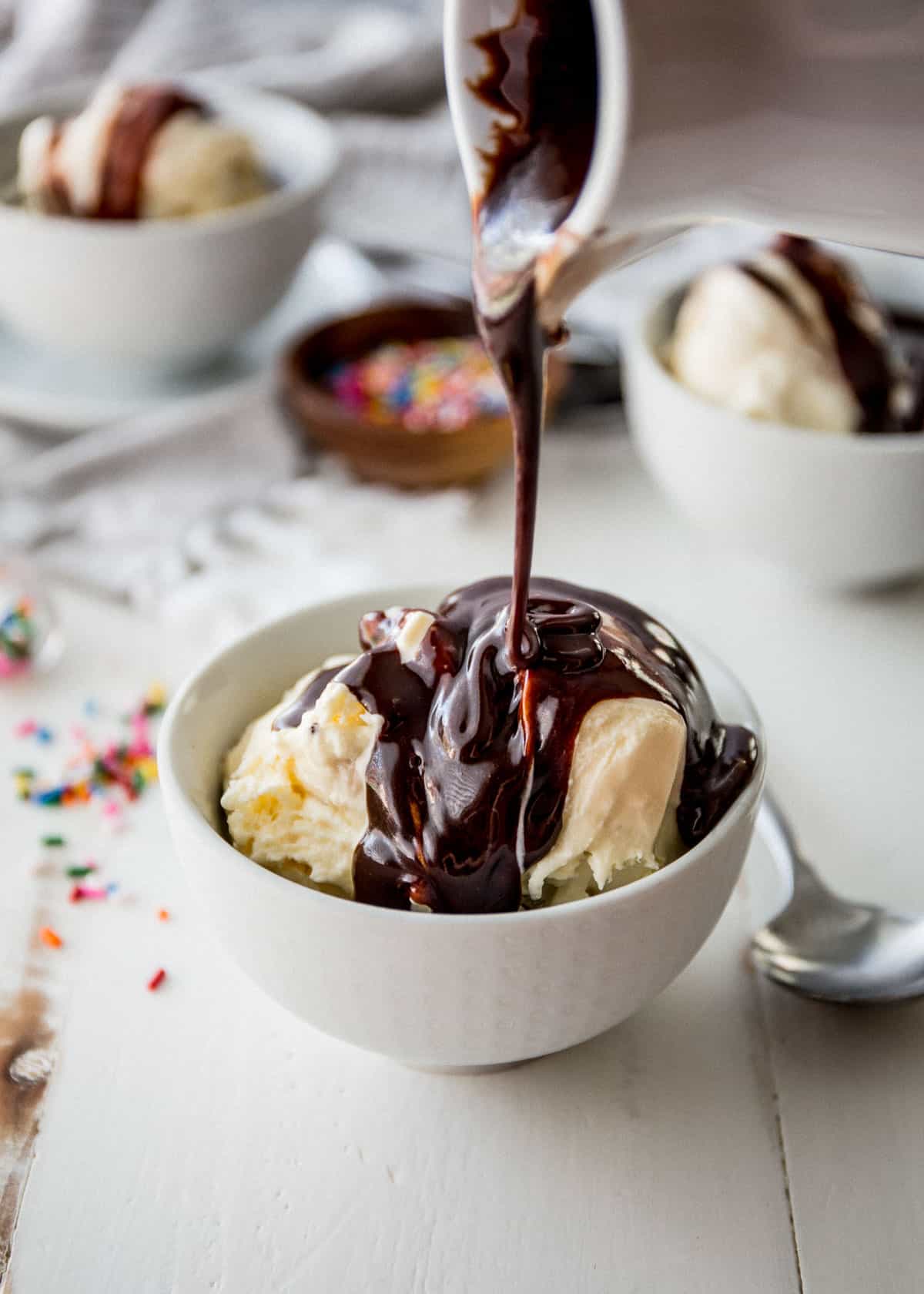 pouring hot fudge over a bowl of vanilla ice cream