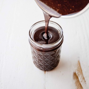 pouring fudge sauce into a small glass jar
