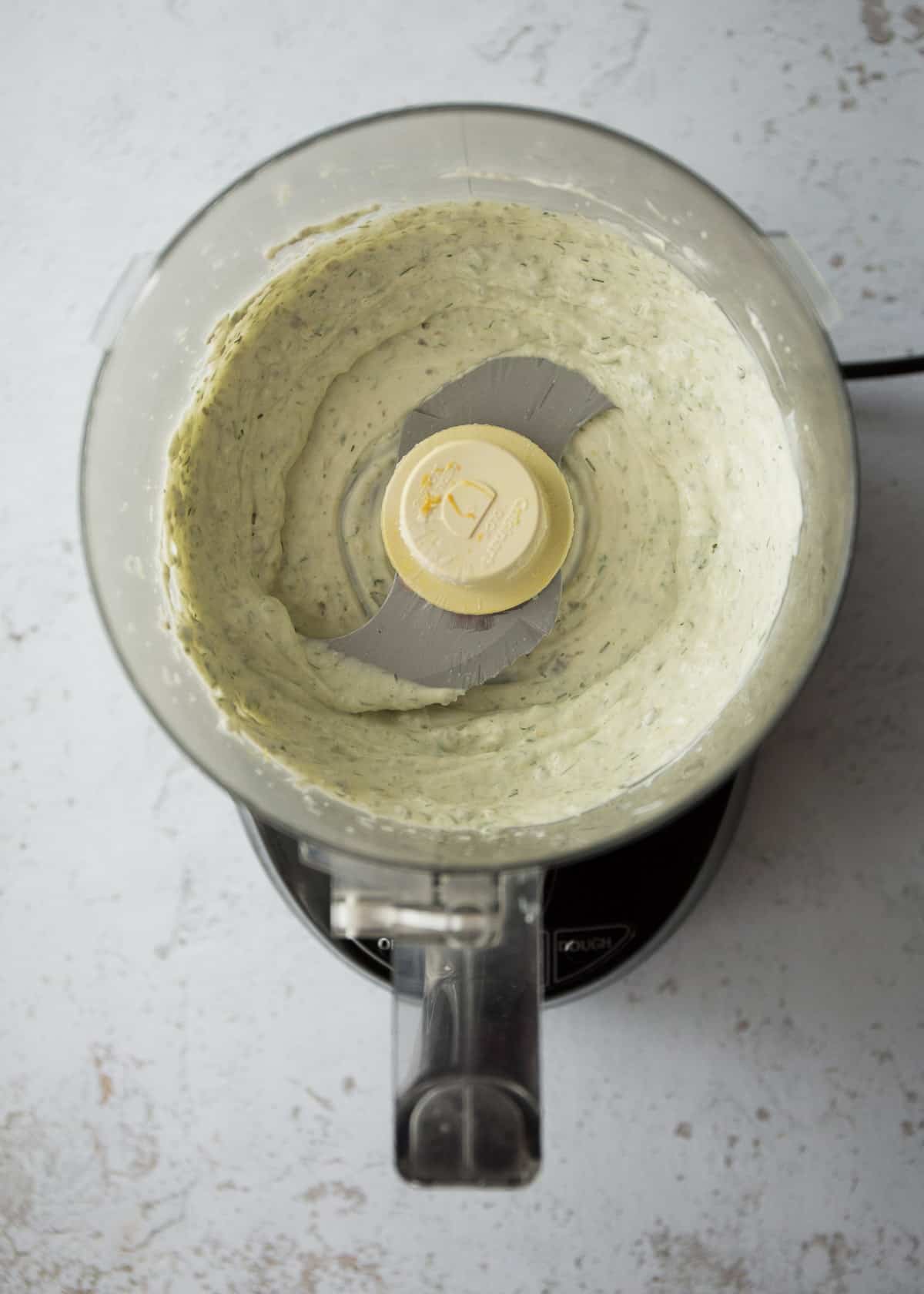 overhead image of herb sauce in the bowl of a food processor