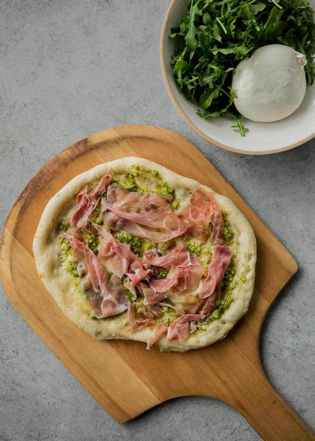 overhead image of a raw homemade pizza on a wooden pizza peel